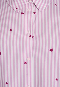 Chemise rayée rose et blanche avec de petits cœurs rouges, col et boutons légers sur le devant. Tissu lisse avec un éclat subtil.