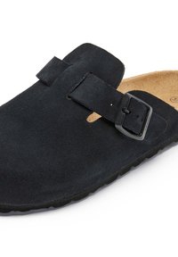 Sabots en daim noir avec une sangle réglable et une boucle en métal. Semelle intérieure contournée couleur tan et semelle en caoutchouc noir. Bout fermé avec des découpes décoratives.