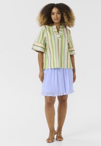 Ribakujund ja pastellroheline lühikeste varrukatega särk, millel on sälkkaelus, koos helesinise volditud seelikuga. Pruunid rihmadega sandaalid.