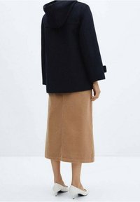 Cappotto con cappuccio blu navy dalla vestibilità rilassata, abbinato a una gonna in corduroy color beige fino al ginocchio e tacchi bianchi con punta affilata.