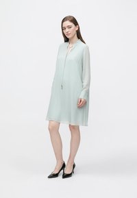 Hellminzgrünes Kleid, kurze Ärmel, gerader Schnitt, mit Kragen und Reißverschluss vorne. Kombiniert mit schwarzen spitzen High Heels. Glatter Stoff.