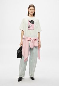 Valge t-särk roosa ja musta graafilise trükiga, hallikas-sinised teksad ning roosa triibuline särk vöö ümber seotud. Must käsikott ja kingad.