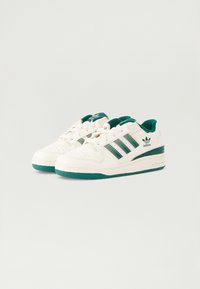 Bijela tenisica s zelenim naglascima, s tri zelena pruga sa strane, podstavljenim jezičkom i teksturiranom gumenom potplatom. Klasičan dizajn niskih tenisica.