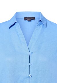 Lichtblauwe overhemd met kraag, gemaakt van een gestructureerde stof. Heeft een v-hals en vier bijpassende knopen aan de voorkant.