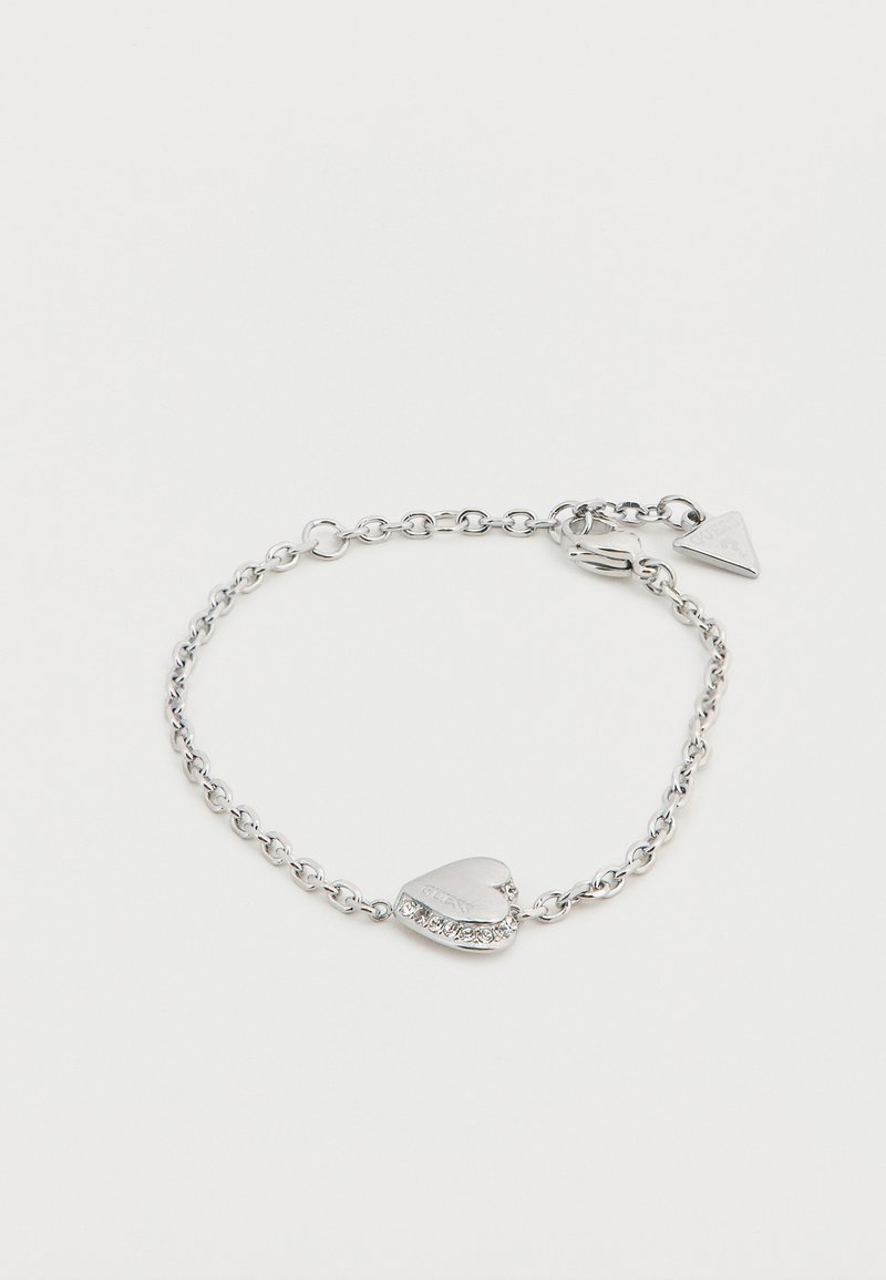 Bracelet chaîne en argent avec un pendentif en forme de cœur orné d'un cristal et d'un détail gravé. Fermoir simple avec une étiquette triangulaire attachée.