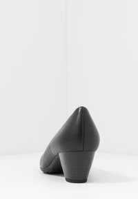 Svart lädersko med klack, spetsig tå, låg klack och slät yta. Inga synliga mönster eller metallaccenter.