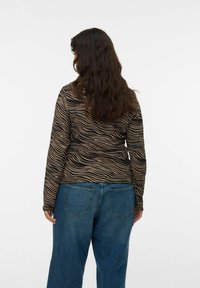 T-shirt à manches longues avec un motif ondulé noir et tan, associé à un jean en denim bleu ample avec poches arrière. Texture douce, coupe décontractée.