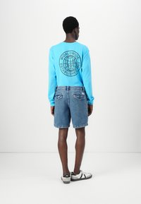 Light blue long-sleeve shirt with black graphic design on the back, paired with denim shorts and black-and-white sneakers.