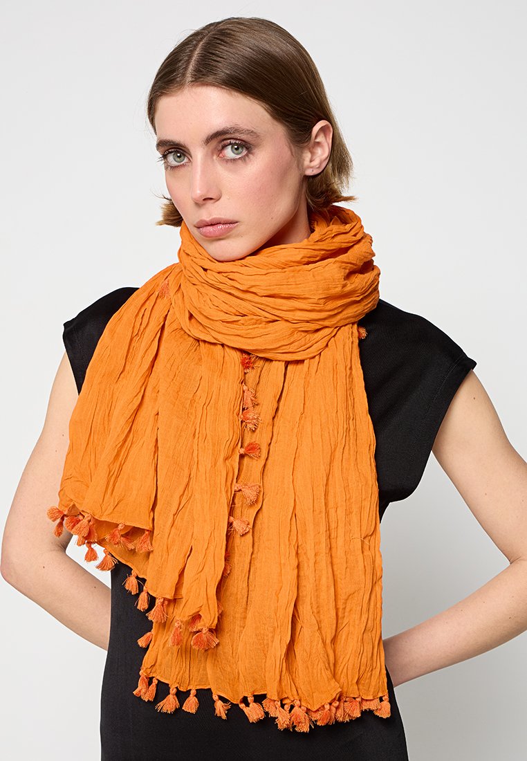 Pomarańczowy, marszczony szalik z frędzlami na krawędziach. Lekka tkanina, luźno owinięta, ukazująca teksturowany, warstwowy design.