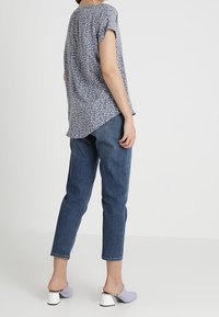 Haut à manches courtes à motif floral bleu marine, associé à un jean en denim bleu taille haute et des mules à talons blocs lilas.