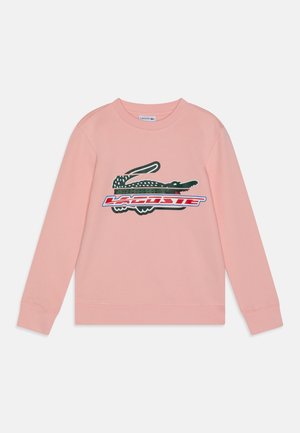 Sudadera de algodón rosa con mangas largas, cuello acanalado y un gran gráfico de un cocodrilo con la palabra "LACOSTE" en rojo y azul.