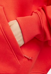 Sudadera roja con un tejido texturizado, puños acanalados y un bolsillo frontal con un detalle de ajuste mediante cordón.