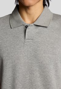 Polo gris en mélange de coton, avec un col classique, une patte de boutonnage à deux boutons et un logo en relief sur la poitrine.