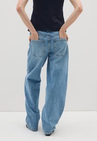 Jeans in denim azzurro chiaro a gamba larga con vita alta, caratterizzati da due tasche posteriori e una vestibilità rilassata. Il tessuto ha una texture morbida e un effetto sbiadito.