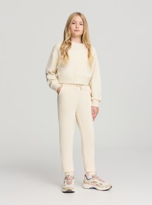 Completo casual color crema composto da una felpa corta e pantaloni sportivi a vita alta con fondo stretto. Il materiale è morbido con una texture liscia.