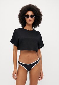 T-shirt cropped nero con maniche corte, abbinato a bikini bottoms neri con accenti bianchi. Tessuto dalla trama liscia.