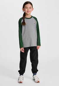 Grå långärmad t-shirt med gröna ärmar, med en liten logotyp. Matchas med svarta joggers och vita sneakers med gröna detaljer.