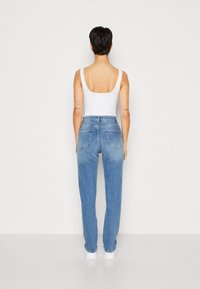 Jeans de tiro alto en un azul claro con un ajuste relajado, que cuentan con dos bolsillos traseros y un ligero desgastado hacia la parte inferior. Llevados con una camiseta sin mangas blanca.