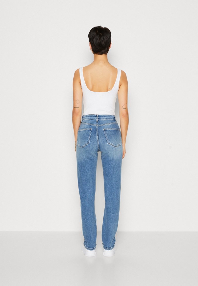 Jeans de tiro alto en un azul claro con un ajuste relajado, que cuentan con dos bolsillos traseros y un ligero desgastado hacia la parte inferior. Llevados con una camiseta sin mangas blanca.