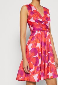 Robe à imprimé floral dans des tons rose, violet et rouge. Dotée d'un design portefeuille avec un col en V et une jupe évasée. Fabriquée en tissu léger.