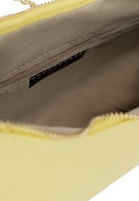 Gelbe Leder-Clutch mit glatter Textur, ausgestattet mit einem goldenen Reißverschluss und beiger Stoffauskleidung, die das Innenfach und das Etikett zeigt.