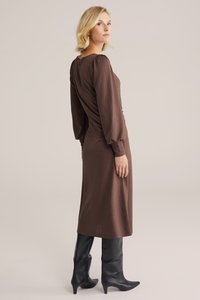 Brązowa, teksturowana sukienka midi z bufiastymi rękawami i marszczeniem z tyłu, zestawiona z czarnymi, sięgającymi do kolan botkami na obcasie.