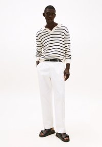 Striped sweater in cream and navy, white trousers, black belt, and sandals. Slim fit, long sleeves, V-neckline, and textured fabric.