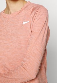 Ljusorange tröja med strukturerat mönster, med rund halsringning och en liten vit Nike-logga på bröstet.