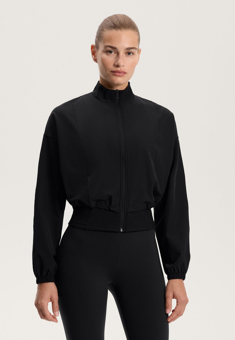 Černá zipová bunda s vysokým límcem, elastickými manžetami a zkráceným lemem. Vyrobena z hladké tkaniny, má strukturovaný design.