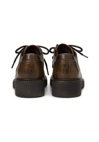 Chaussures en cuir marron à lacets avec des semelles épaisses noires, vues de l'arrière montrant le logo embossé sur chaque talon.