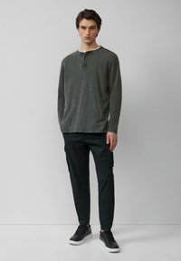 Ciemnozielona koszula z długim rękawem i zapięciem na guziki, sparowana z czarnymi spodniami cargo i czarnymi sneakersami. Gładka tekstura i luźny krój.