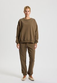Brown cotton oversized sweatshirt with dropped shoulders and a round neck, paired with matching tapered pants and light-colored slip-on shoes.
