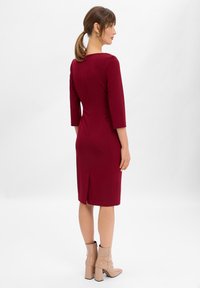 Abito fitted color marsala con maniche a tre quarti, zip sul retro e lunghezza a ginocchio, abbinato a stivaletti ankle boots beige con tacco a blocco.