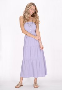 Hellblau-lila, gestuftes Maxikleid aus strukturiertem Stoff, mit einem knopfartigen Oberteil und Spaghettiträgern. Kombiniert mit metallic Sandalen.