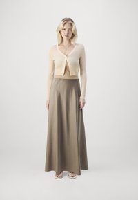 Beige ribbed cardigan with a cropped design and long sleeves, paired with a flowing, olive green satin maxi skirt. Sandals are visible.