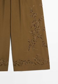 Brown fabric with embroidered floral patterns along the hem and side, showing detailed leaves and flowers in matching thread.