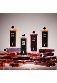 Cinque bottiglie di profumo rettangolari di vari colori (arancione, rosa, trasparente, lavanda) con tappi neri arrotondati, dotate di etichette nere con testo bianco.