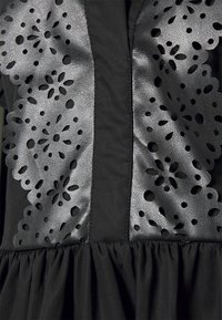 Svart klänning med en perforerad läderfrontpanel med blommönster, kompletterad med en rynkad nederkant av tyg.