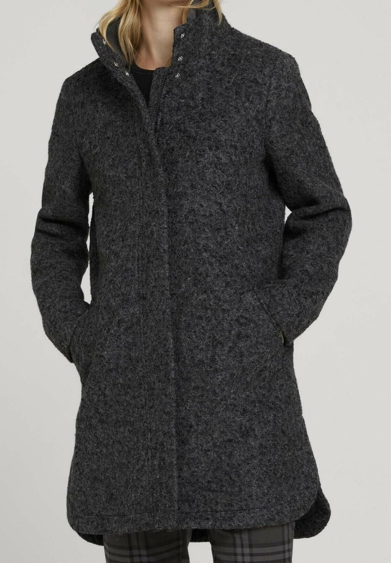 Cappotto grigio in misto lana con collo alto, chiusura a bottoni a pressione, due tasche laterali e finitura testurizzata. Il design è di lunghezza media e foderato.