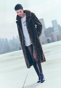 Leopardprint faux fur frakke, børstet tekstur, bred krave; båret over en hvid grafisk t-shirt og parret med sorte knæhøje støvler.