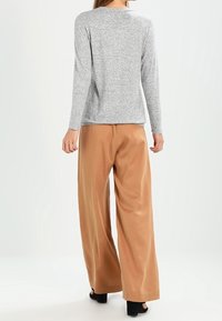 Top gris de manga larga con tejido texturizado, combinado con pantalones anchos marrones. El dobladillo recto y el corte relajado ofrecen comodidad y facilidad.