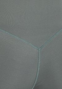 Legginsy o wysokim stanie, elastyczne w stonowanym odcieniu teal. Posiadają płaskie szwy i gładkie, matowe wykończenie. Brak widocznego logo lub wzoru.