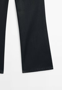 Pantalon large noir en tissu lisse, présentant un design épuré sans motifs visibles, avec des coutures droites et des bords ourlés.