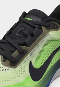 Κοντινή λήψη μαύρου και νέον πράσινου παπουτσιού Nike για τρέξιμο με υφή από δίχτυ, μαύρα κορδόνια και μέρος της σόλας ορατό.
