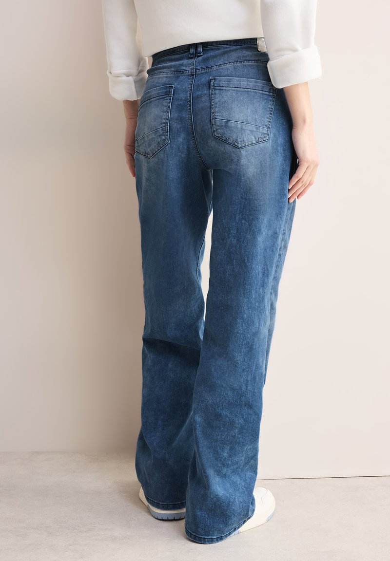 Jeans de mezclilla azul claro con un corte relajado, bolsillos traseros visibles y una textura ligeramente deslavada. Presentan una cintura estándar y piernas ajustadas.