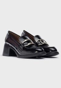 Zapatos de charol negro con tacón cuadrado que cuentan con una punta redondeada y una hebilla decorativa de plata en el empeine. Textura suave y diseño de empeine bajo.
