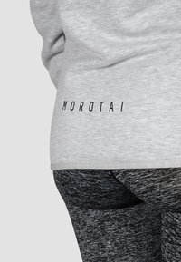 Felpa grigia con una texture sottile, caratterizzata da un logo nero "MOROTAI" all'orlo. Abbinata a leggings neri texture.