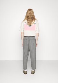 Beżowa koszulka z czarnymi wyrazistymi literami i różową grafiką na plecach; w zestawieniu z szarymi spodniami w paski i oliwkowymi butami wsuwanymi.