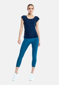 Cămășuță sport cu mânecă scurtă de culoare bleumarin, asortată cu colanți capri de culoare teal. Purtați cu adidași albi, subliniază un design sportiv, ajustat.
