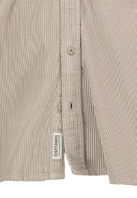 Beiger Cordstoff mit vertikalen Rippungen, Knopfleiste mit drei Knöpfen und einem kleinen rechteckigen Stoffmarkierungsetikett nahe dem Saum.